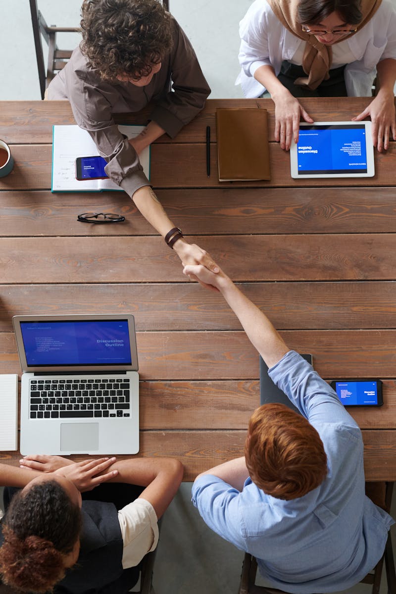 Overhead view of colleagues in a work meeting using laptops and tablets, emphasizing teamwork and technology.